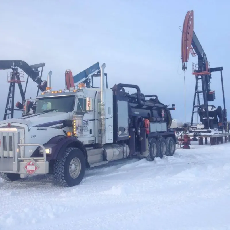 A Troyer vac truck in the snow between two pumpjacks
