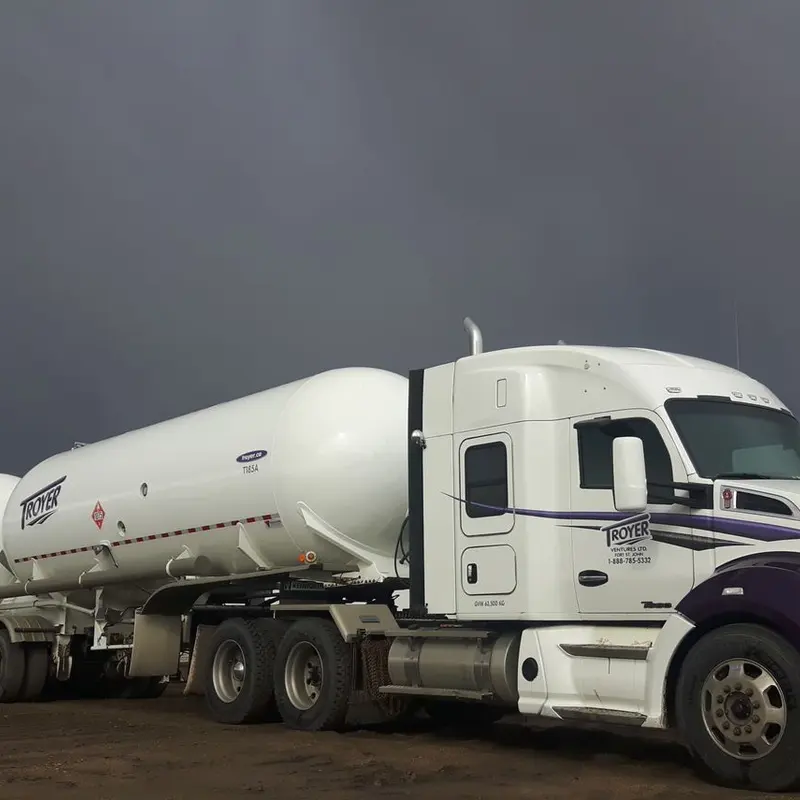 A Troyer tractor with white tank trailers under a grey sky
