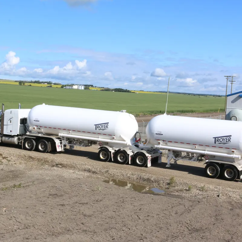 White tank trailers lettered TROYER beside a green field