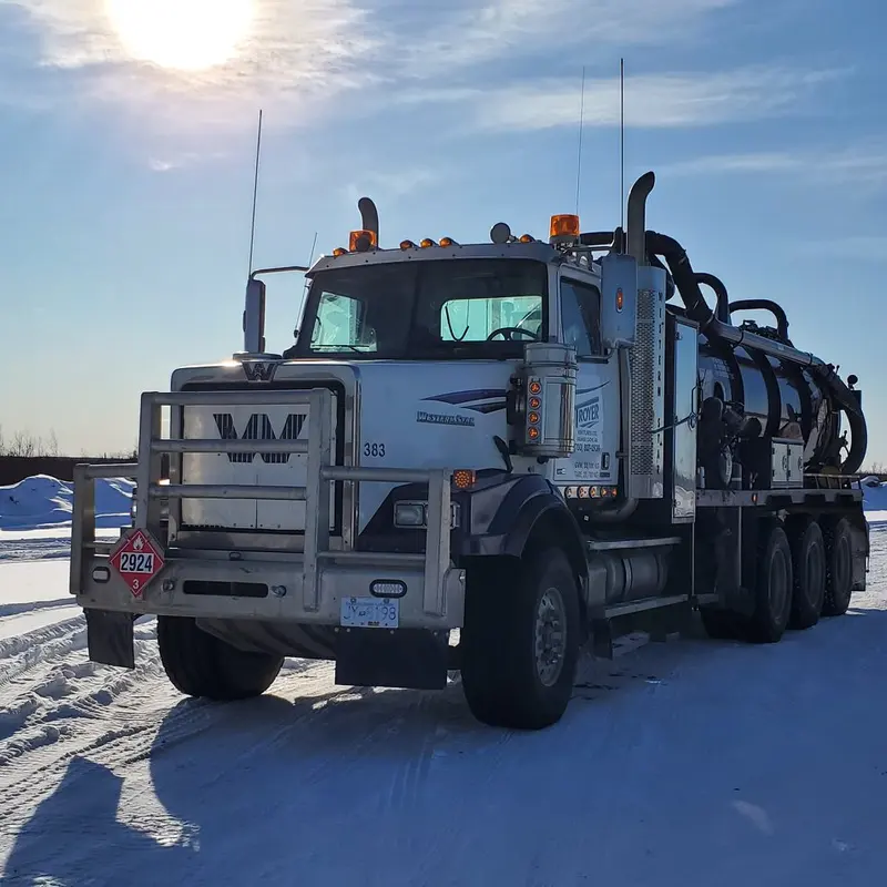 A Troyer vac truck on a snow-covered field with the sun low behind it