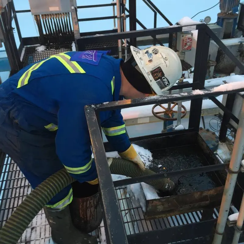 A worker in coveralls and a hard hat guiding a vac hose into a sump