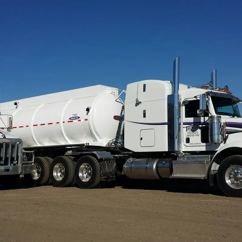 A Troyer tractor with a white tank trailer under a deep blue sky