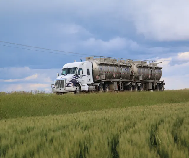 A Troyer B-train tanker on a road above a green wheat field