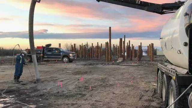 A Troyer vac truck boom reaching down to a worker at a site with rows of steel piles at dawn