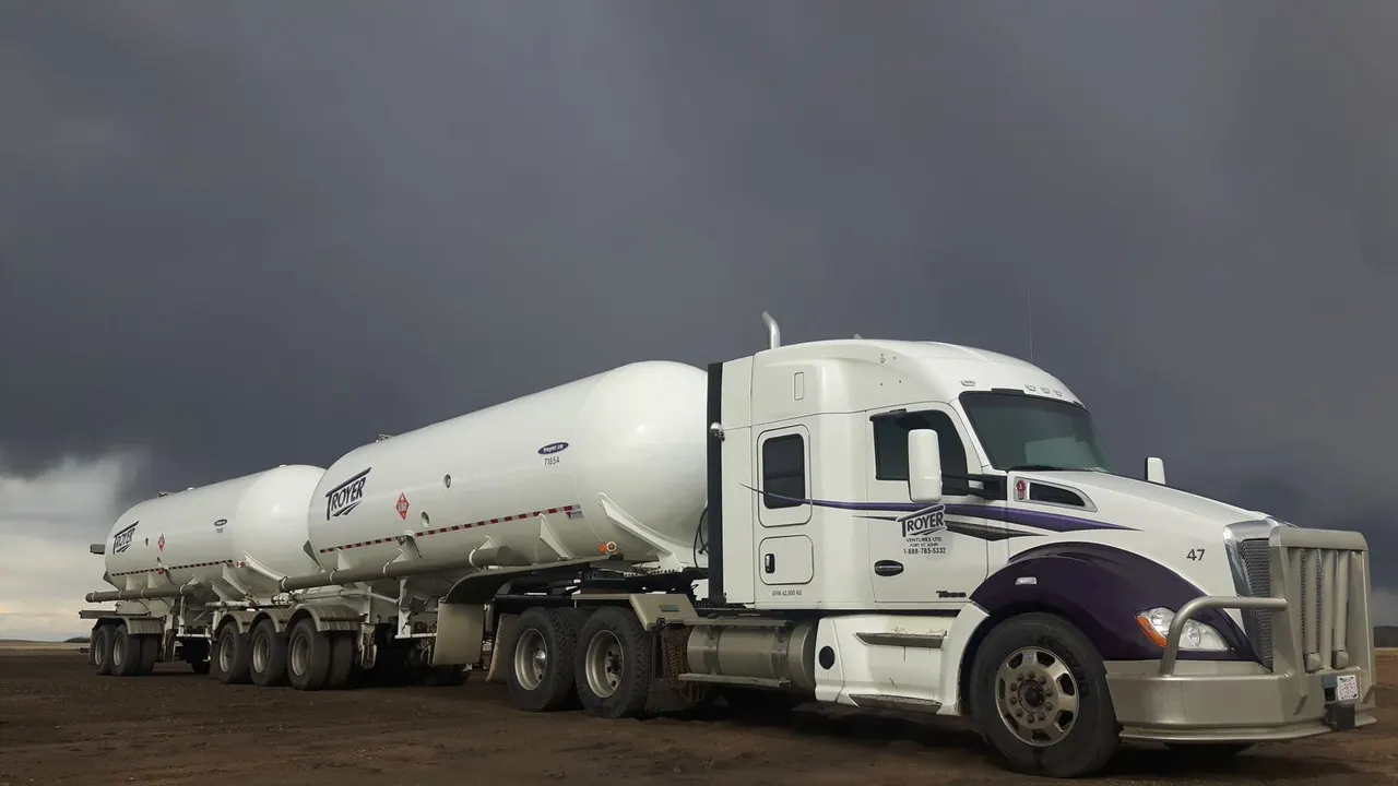 A Troyer tractor pulling white TROYER tank trailers under a dark sky
