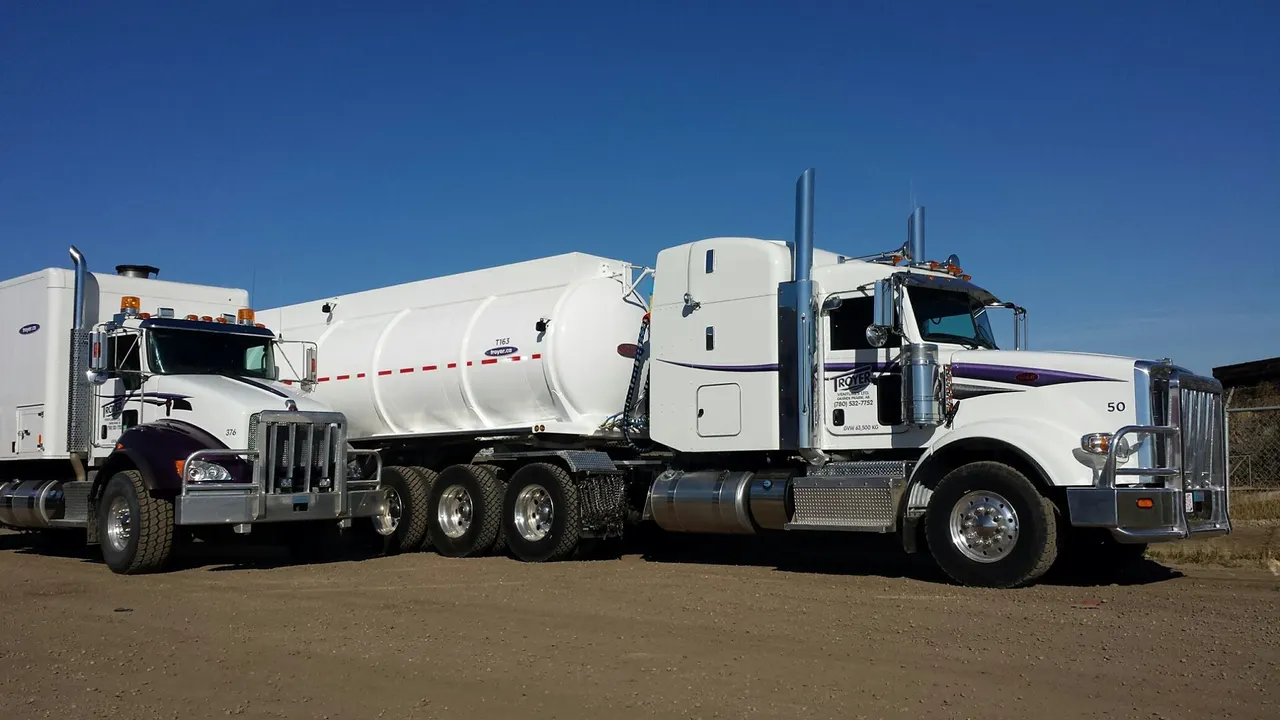 A Troyer tractor with a white tank trailer under a deep blue sky